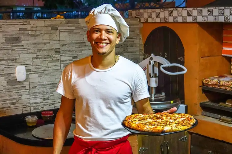 Pizzaiolo souriant qui présente une pizza devant son four